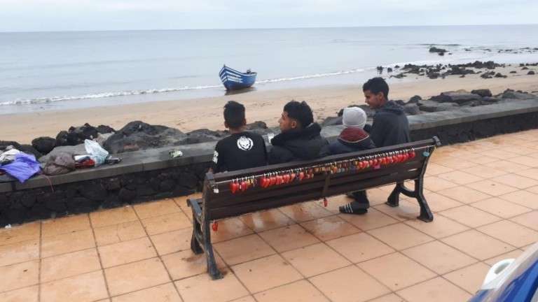 Cuatro de los migrantes que llegaron a Matagorda, con la patera al fondo (Foto TA)