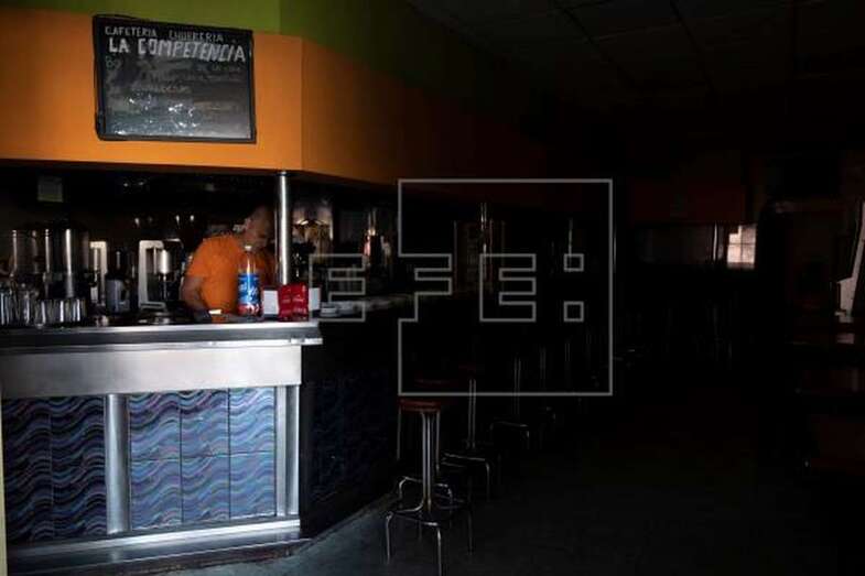 Un empleado de cafetería de Santa Cruz de Tenerife intenta trabajar a oscuras mientras espera que se restablezca el suministro eléctrico (Foto Efe / Miguel Barreto)