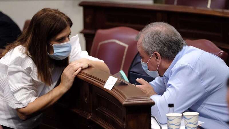 La diputada y vicealcaldesa de Telde, Carmen Hernández, charla en el Parlamento canario con su compañero de partido Luis Campos, ambos con mascarillas (Foto TA)