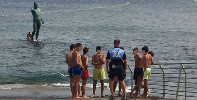Un agente de la Policía Local advierte a un grupo de niños del peligro de encaramarse a la figura de Neptuno (Foto TA)
