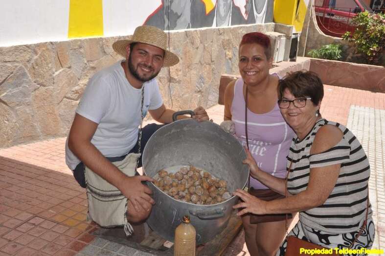 Estiven Bolaños, presidente de la comisión de fiestas, y dos vecinas de La Viña sostienen un caldero de papas arrugadas (Foto Teldeenfiestas)