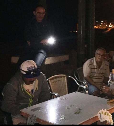 Los jugadores de cartas usan linternas para alumbrarse porque las farolas próximas están inoperativas (Foto TA)