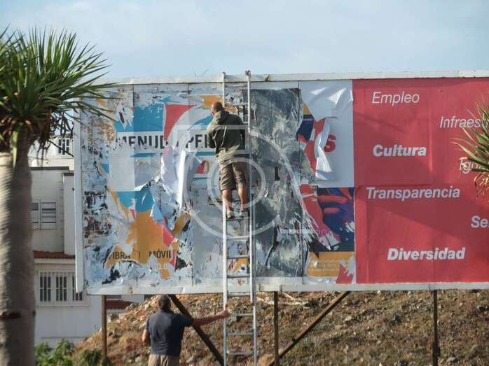 Momento en que dos operarios de una empresa de publicidad retira el cartel electoral del PSOE de la valla situada detrás de Leroy Merlin (Foto TA)