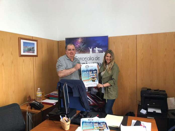 El edil Juan Martel y una representante del colegio posan junto al cartel de la gala (Foto TA)