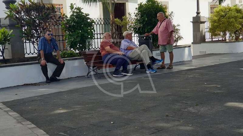 Grupo de personas sentadas en uno de los pocos bancos que están a la sombra en la plaza (Foto TA)